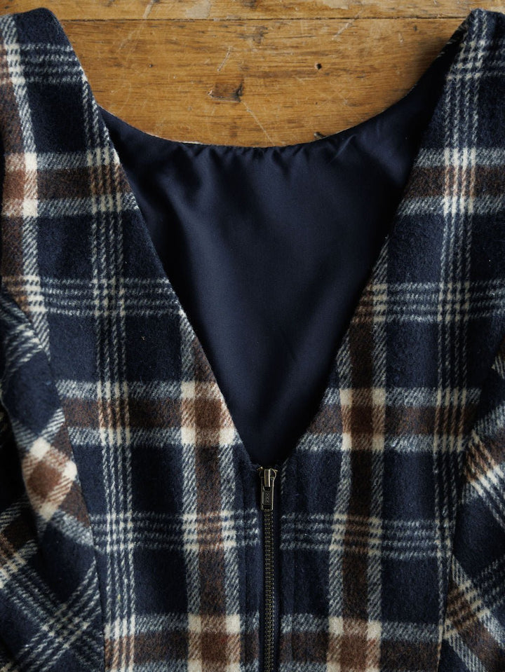 Close-up of the Mondovi Flannel Dress by Savannah Sevens western life{&}style: navy blue, brown, and white plaid with a black zipper, solid dark blue lining, displayed on a wooden surface.