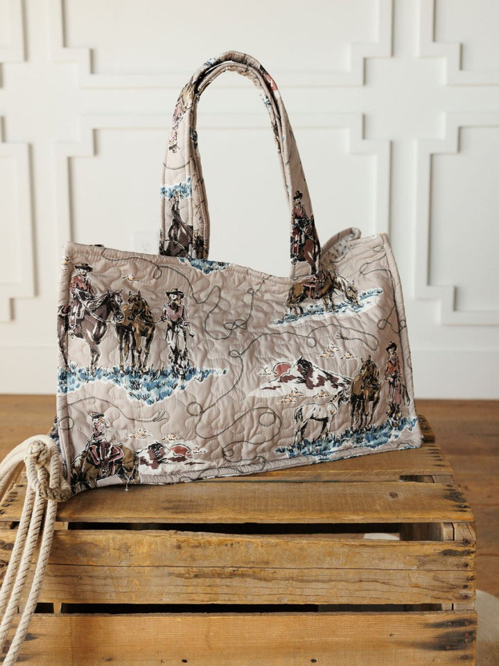 The Montana Summer Collection by Savannah Sevens western life&style features a handmade quilted bag set with cowboy and horse prints, shown on a crate with rope against a white paneled wall, highlighting its unique western style.
