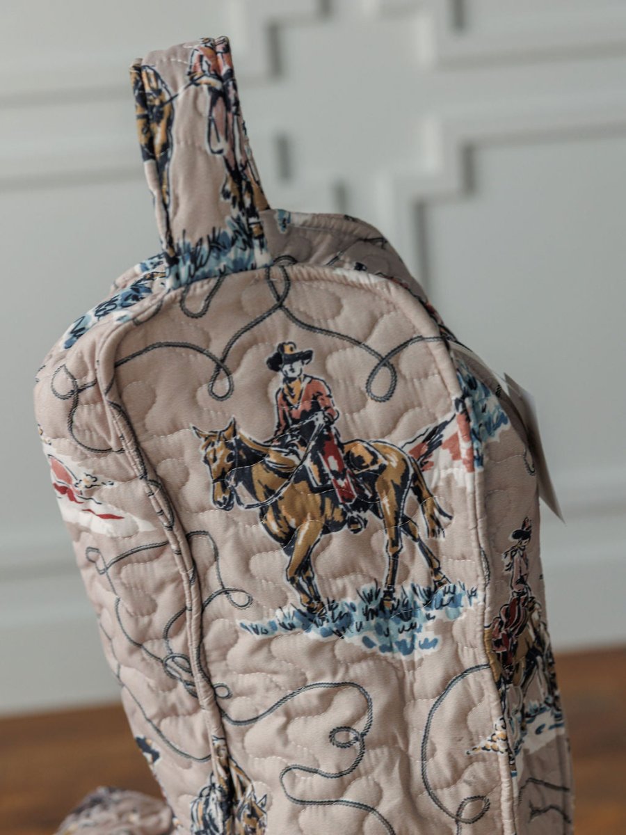 The Montana Summer quilt bag by Savannah Sevens western life{&}style features a cowboy and horse pattern on light beige with blue and brown accents. Shown from the side, the bag includes a top handle and is part of our western collection.