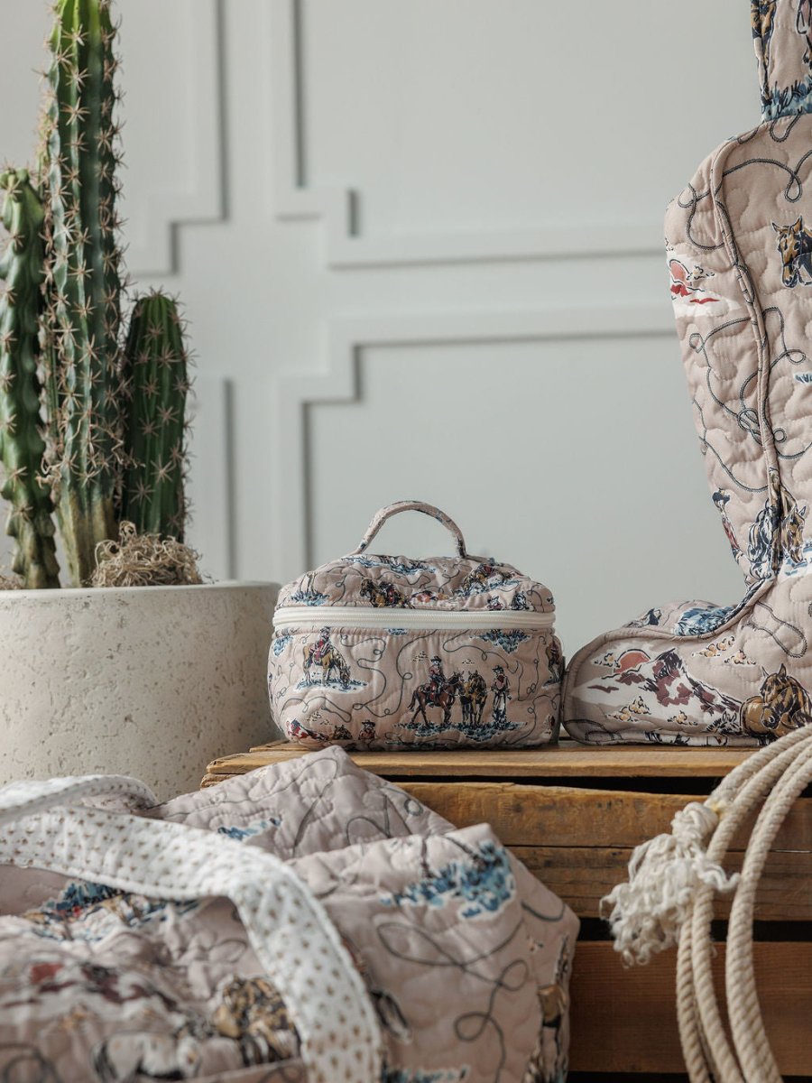 Soft quilted bags and a small box with whimsical prints from the Montana Summer Collection by Savannah Sevens western life&style are arranged on wood beside a tall cactus, set against a textured white wall.