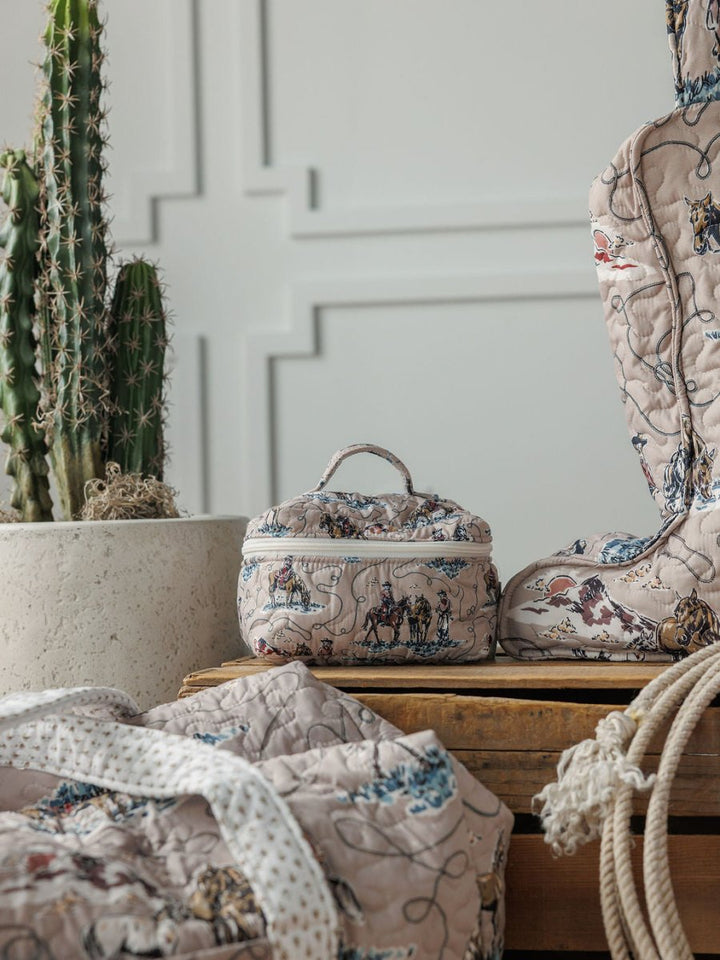 Soft quilted bags and a small box with whimsical prints from the Montana Summer Collection by Savannah Sevens western life&style are arranged on wood beside a tall cactus, set against a textured white wall.