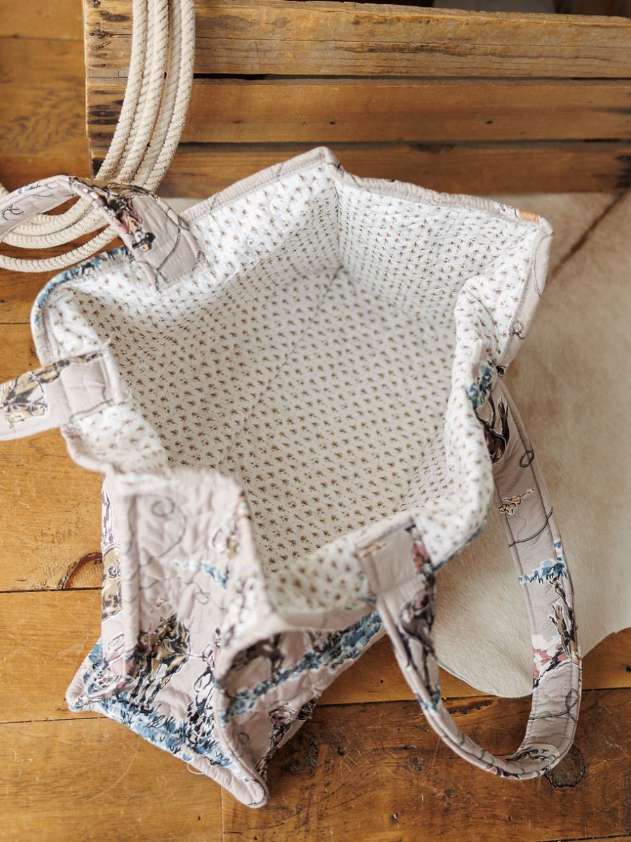 The Montana Summer Collection fabric tote bag by Savannah Sevens western life&style, featuring a light floral lining and spacious interior, sits open on wood beside coiled rope and white hide.