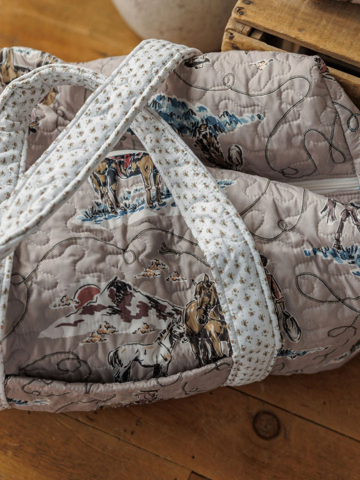 The Montana Summer Collection bag by Savannah Sevens western life&style features a Western horse and cowboy print, white handles, and is shown on a wooden floor beside a crate.