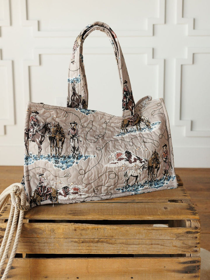 The Montana Summer Collection by Savannah Sevens western life&style features a handmade quilted bag set with cowboy and horse prints, shown on a crate with rope against a white paneled wall, highlighting its unique western style.