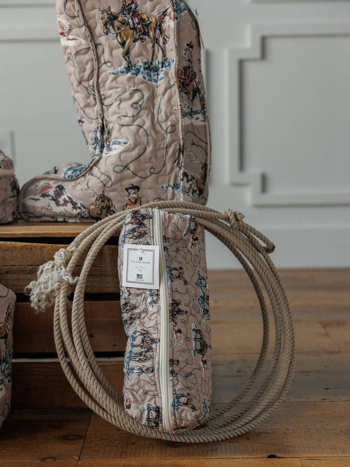 The Montana Summer Collection by Savannah Sevens western life&style features a quilted bag set with cowboy and horse motifs, set on a wooden floor beside a matching piece. A white label accents the zipper, all against a white paneled wall.