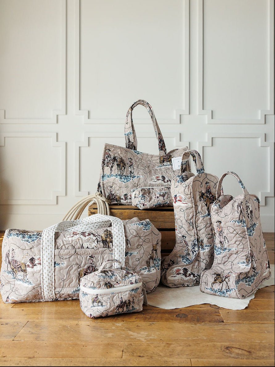 Five quilted travel bags and boots with a vintage map print from the Montana Summer Collection by Savannah Sevens western life&style are displayed on a wooden floor in front of a white paneled wall.