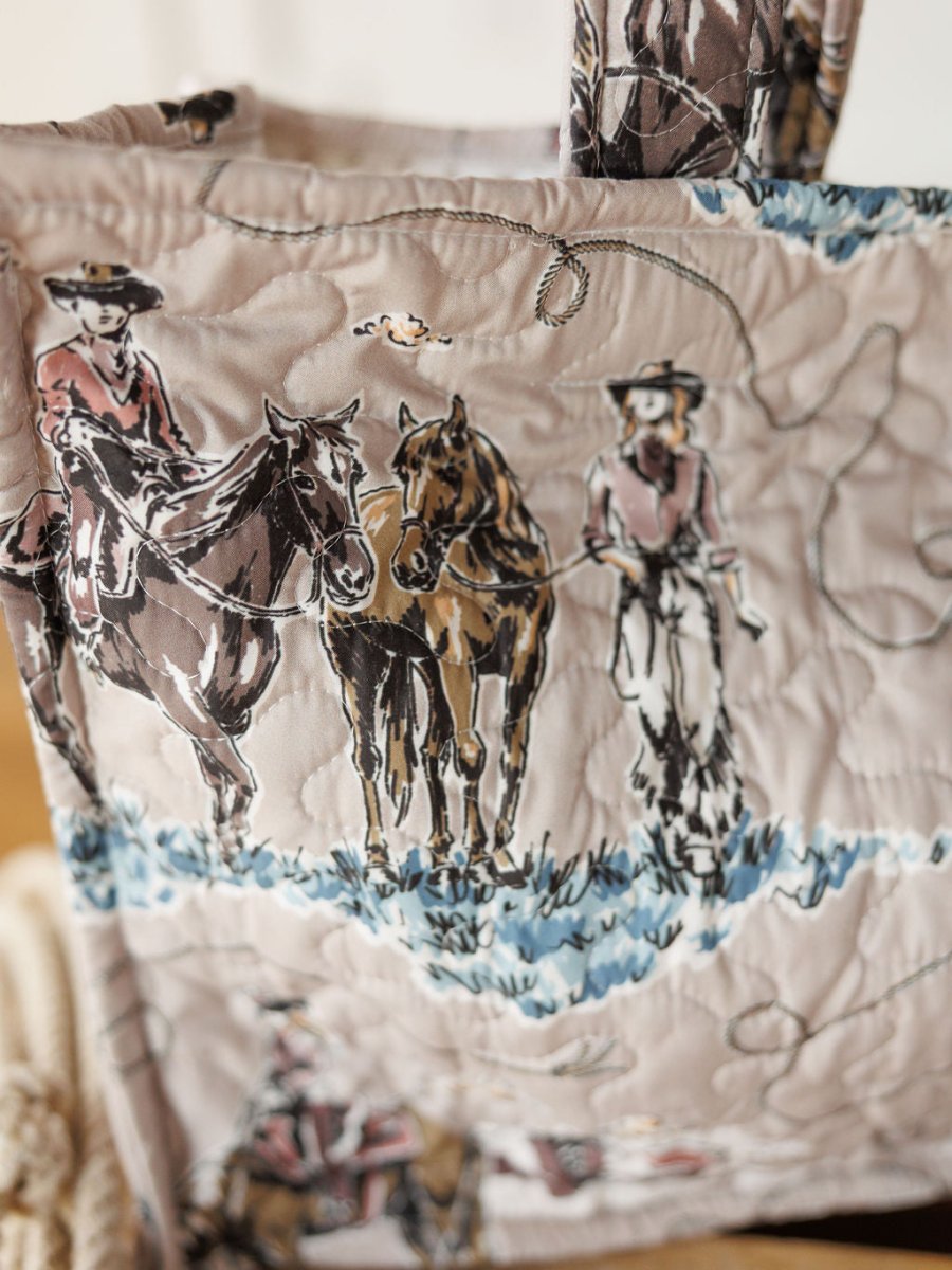 A close-up of quilted fabric from the Montana Summer Collection by Savannah Sevens western life&style, featuring cowboys on horses in brown, blue, and pink. Ideal for handmade quilts or quilted bag sets.
