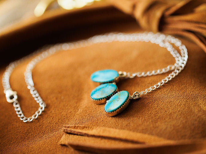 The Montrose Necklace by Savannah Sevens western life{&}style features three oval Red River Turquoise pendants in sterling silver, displayed on a soft brown suede surface.