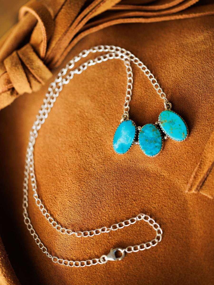 The Montrose Necklace by Savannah Sevens western life{&}style features three oval Red River Turquoise stones set in sterling silver, displayed on brown suede with a bow detail.