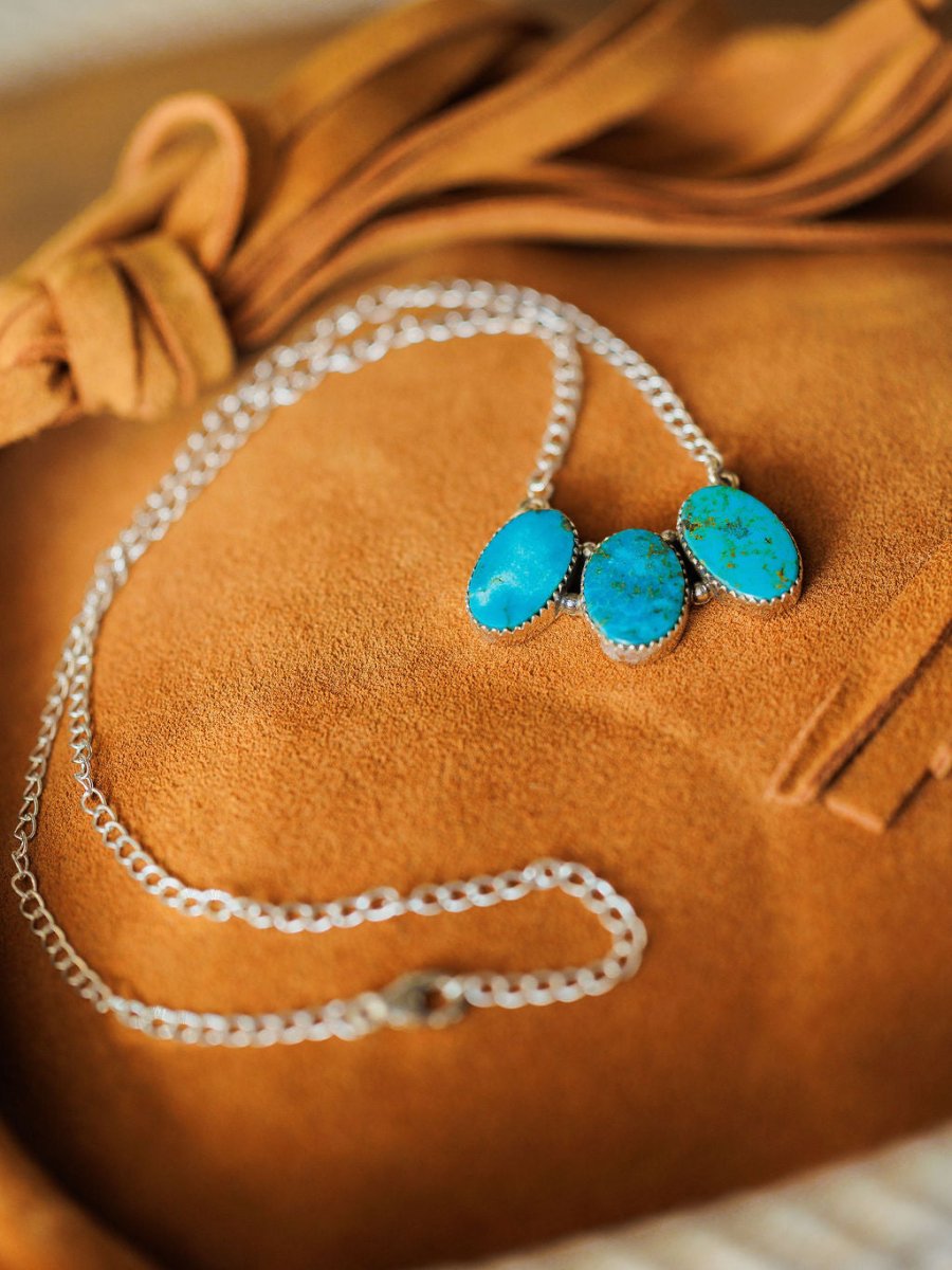 The Montrose Necklace by Savannah Sevens western life{&}style features three oval Red River Turquoise stones, elegantly displayed on soft tan suede with decorative fringe accents.
