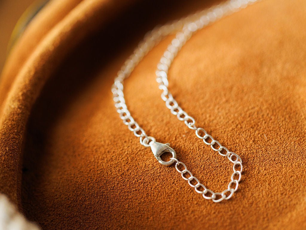 A close-up of the Montrose Necklace by Savannah Sevens western life{&}style, crafted in sterling silver with a lobster clasp, displayed on soft light brown suede.