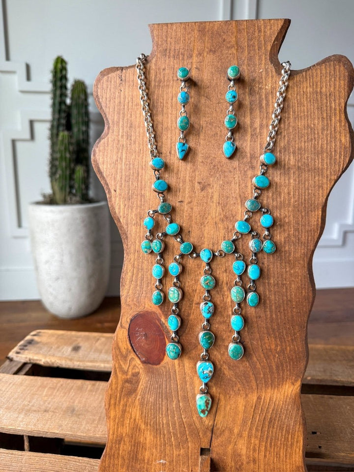 The Morado Necklace & Earrings Set by Savannah Sevens western life&style is showcased on a wooden jewelry bust, with a potted cactus in the background atop a wooden surface and white paneled walls.
