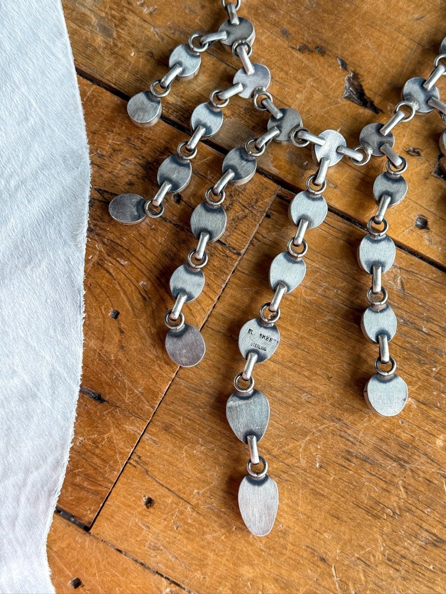 A close-up of the Morado Necklace & Earrings Set by Savannah Sevens western life&style, featuring sterling silver oval and round pieces, displayed on wood beside light cowhide.
