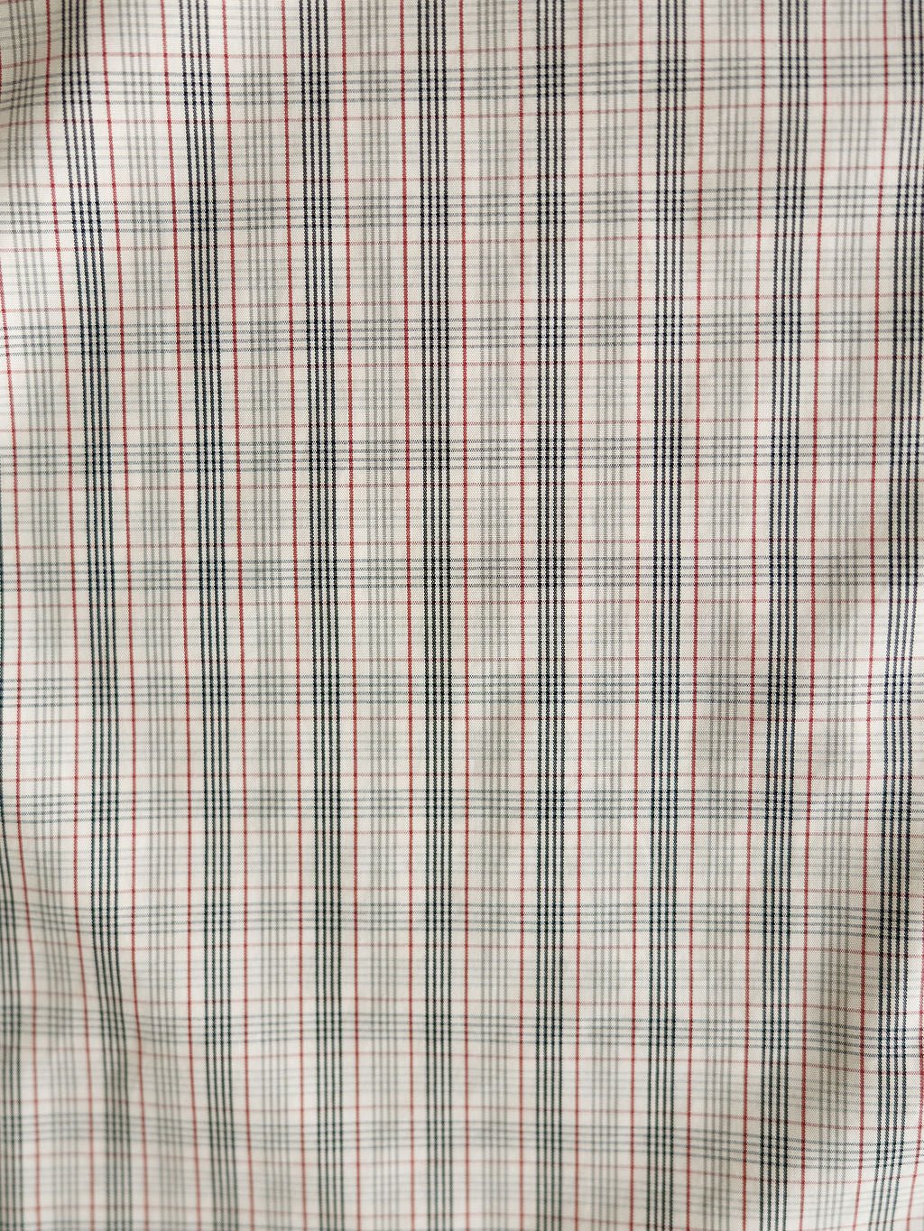 Close-up of the Murtaugh Ariat Men's Natural Plaid Button Up from Savannah Sevens western life{&}style, showing its slightly wrinkled fabric with thin black and red grid lines forming small squares on a white background.