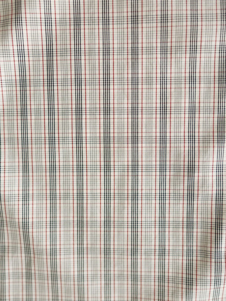Close-up of the Murtaugh Ariat Men's Natural Plaid Button Up from Savannah Sevens western life{&}style, showing its slightly wrinkled fabric with thin black and red grid lines forming small squares on a white background.