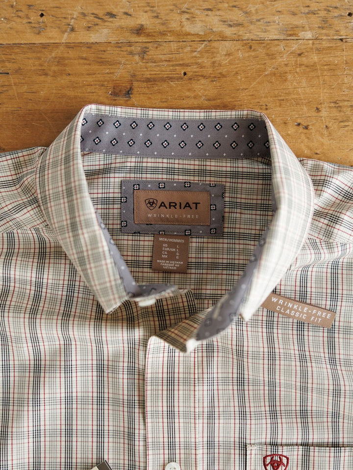 A Murtaugh Ariat Men's Natural Plaid Button Up from Savannah Sevens western life{&}style, featuring a gray patterned inner collar, Wrinkle-Free tags, a chest pocket with red logo, is folded on a wooden surface.
