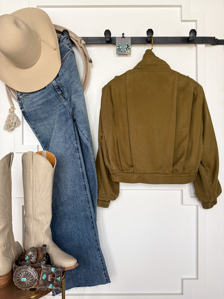 A tan cowboy hat, light brown boots, blue jeans, turquoise earrings, and a brown belt with silver buckles are displayed against a white wall for a classic western-inspired outfit. The look is finished with the Natoma Olive Button Up Jacket by Savannah Sevens western life{&}style, adding a versatile and stylish touch.