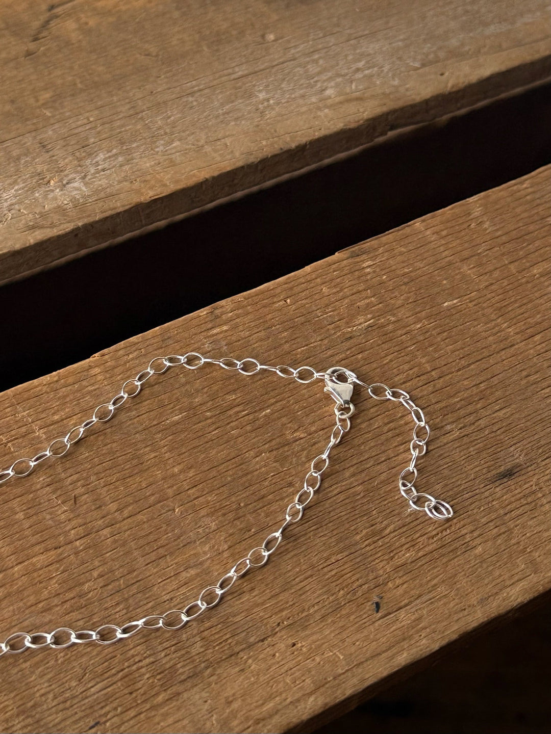 A delicate Navasota Turquoise Bar Necklace by Savannah Sevens western life{&}style with a clasp rests on a rustic wooden surface, with part of the chain extending loosely and unfastened.