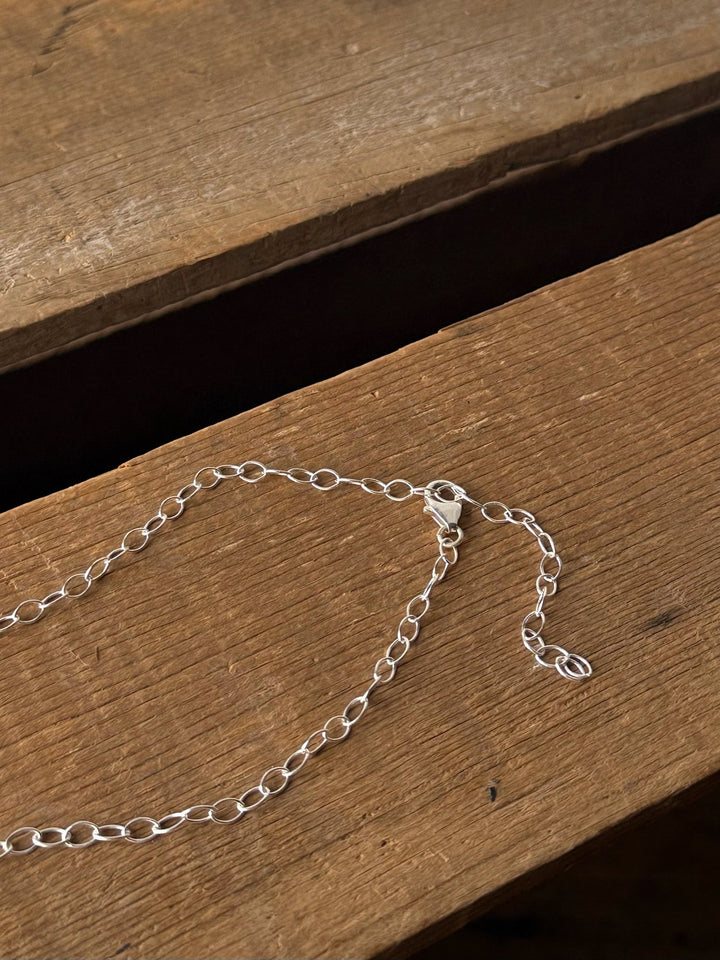A delicate Navasota Turquoise Bar Necklace by Savannah Sevens western life{&}style with a clasp rests on a rustic wooden surface, with part of the chain extending loosely and unfastened.