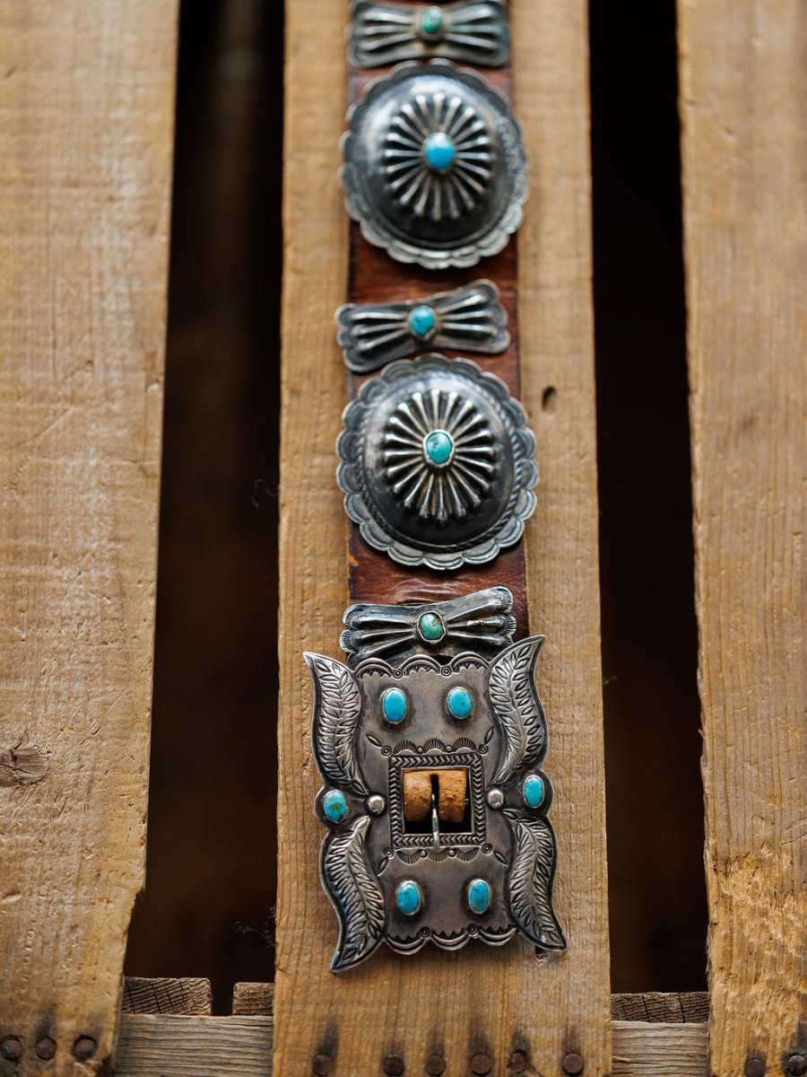 The New Mexico Belt by Savannah Sevens western life{&}style, featuring handmade leather with sterling silver and turquoise details, is displayed on rugged, weathered wooden planks.