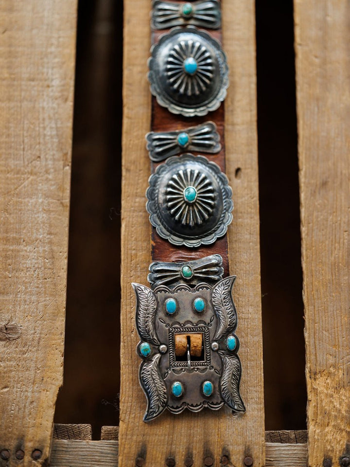 The New Mexico Belt by Savannah Sevens western life{&}style, featuring handmade leather with sterling silver and turquoise details, is displayed on rugged, weathered wooden planks.