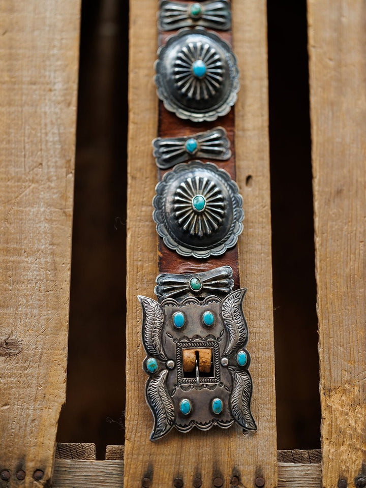 The New Mexico Belt by Savannah Sevens western life{&}style, featuring handmade leather with sterling silver and turquoise details, is displayed on rugged, weathered wooden planks.