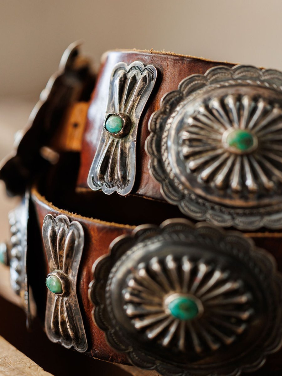 Close-up of the New Mexico Belt by Savannah Sevens western life{&}style, a handmade leather belt with ornate silver conchos, turquoise stones, detailed engravings, and scalloped edges inspired by Southwestern or Native American design.