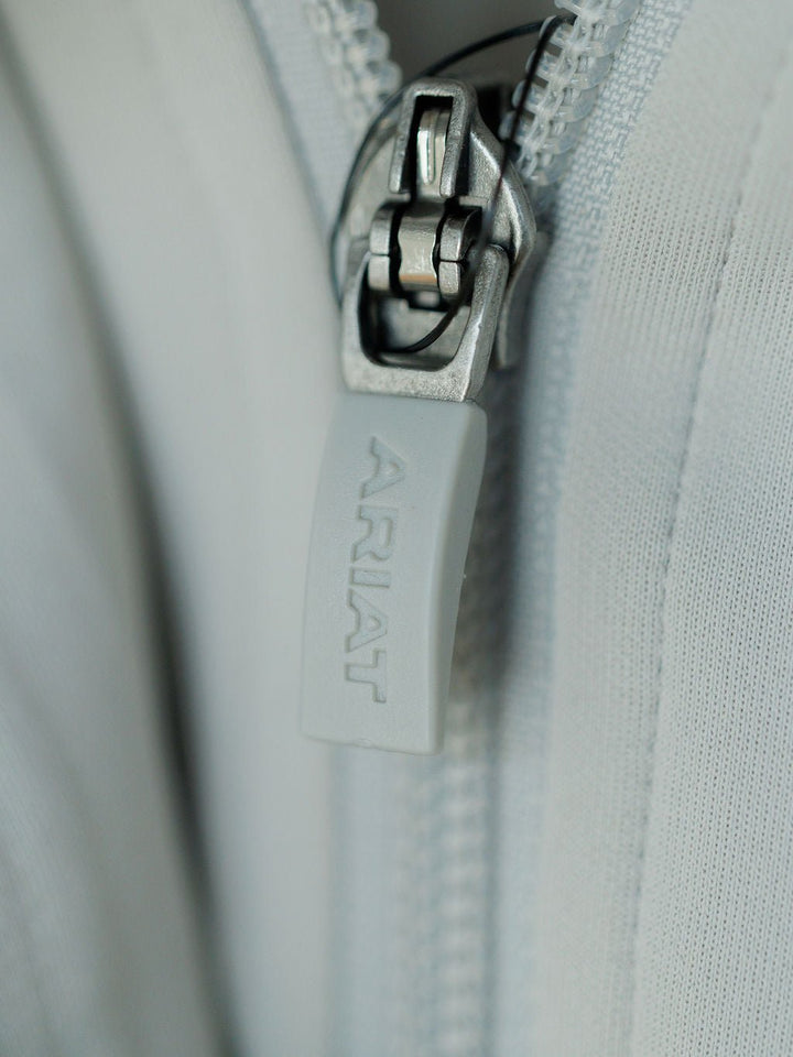 Close-up of the light gray zipper on the Newell Ariat Grey Quarter Zip Pullover by Savannah Sevens western life{&}style, partially open to reveal the fleece lining and textured, moisture-wicking fabric.