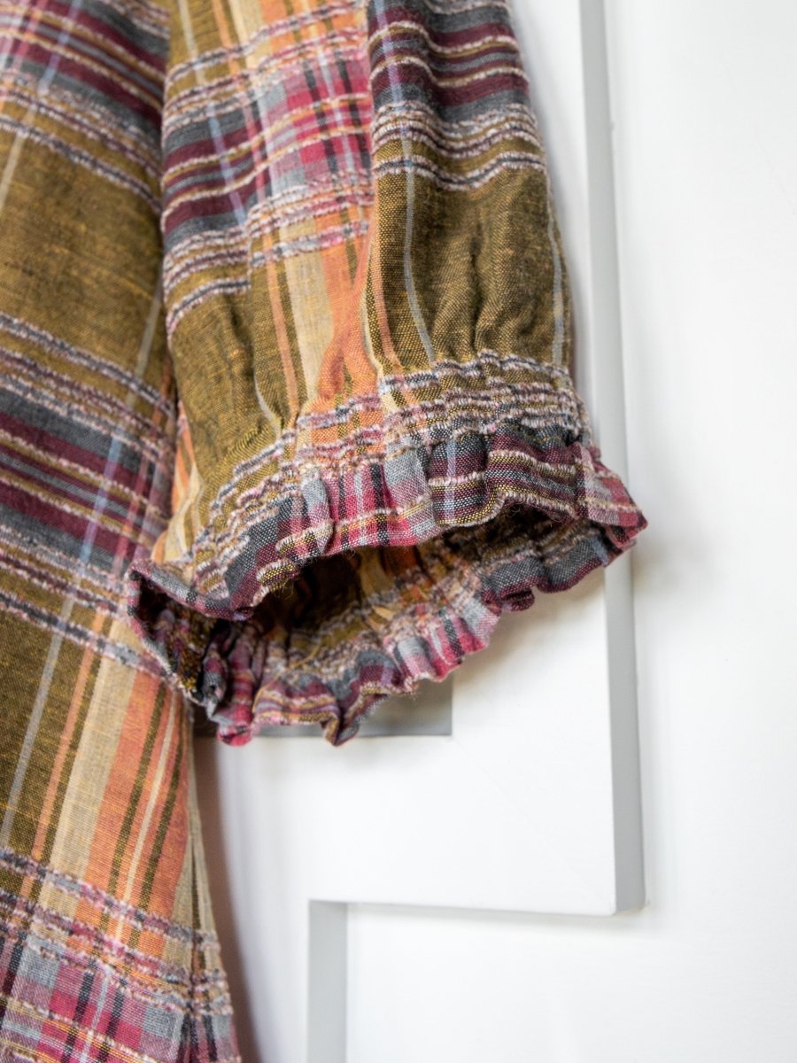 A close-up of the Nicoma Plaid Puff Sleeve Top by Savannah Sevens western life{&}style shows its brown, red, orange, and white plaid fabric with ruffled cuffs, photographed against a white background.