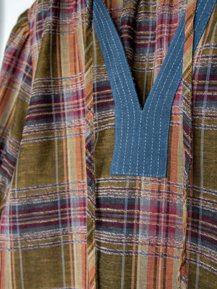 Close-up of the Nicoma Plaid Puff Sleeve Top by Savannah Sevens western life{&}style, showing olive plaid in red, yellow, and green with a deep blue V-stitched neckline detail.
