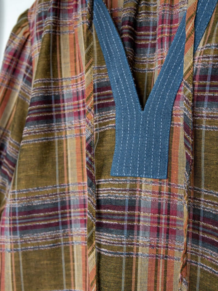 Close-up of the Nicoma Plaid Puff Sleeve Top by Savannah Sevens western life{&}style, showing olive plaid in red, yellow, and green with a deep blue V-stitched neckline detail.