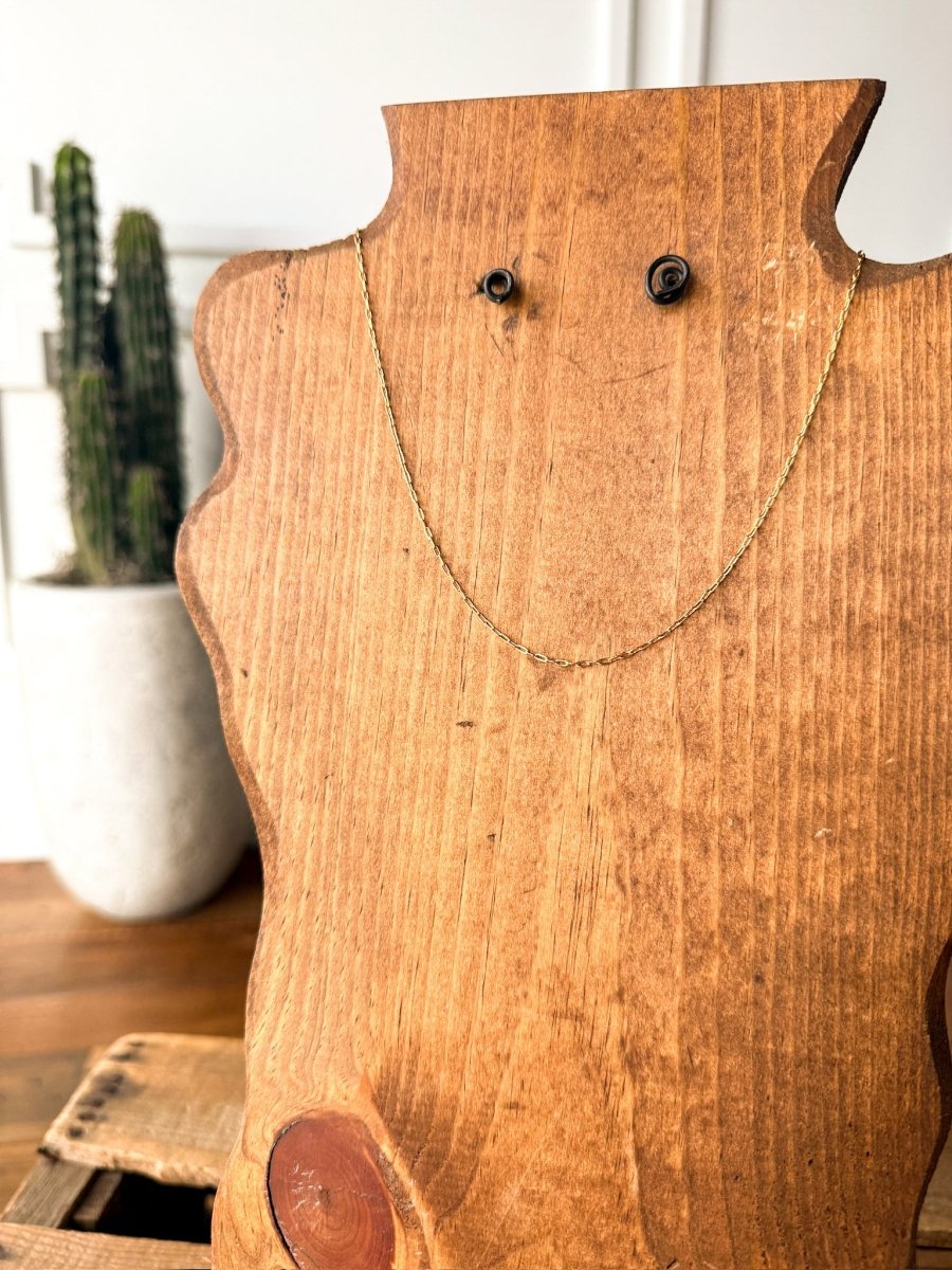The Niota Necklace by Savannah Sevens western life{&}style, a delicate 14k gold filled oval link chain, is shown on a wooden mannequin bust with a blurred potted cactus in the background on a wooden surface.