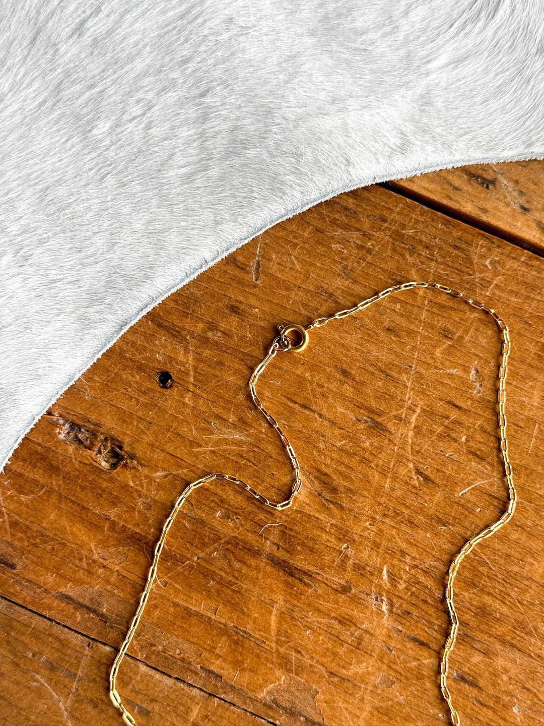 The Niota Necklace by Savannah Sevens western life{&}style features a delicate, tarnish-resistant 14k gold filled oval link chain with clasp, displayed on rustic wood beside soft gray cowhide—adding elegance to any style.