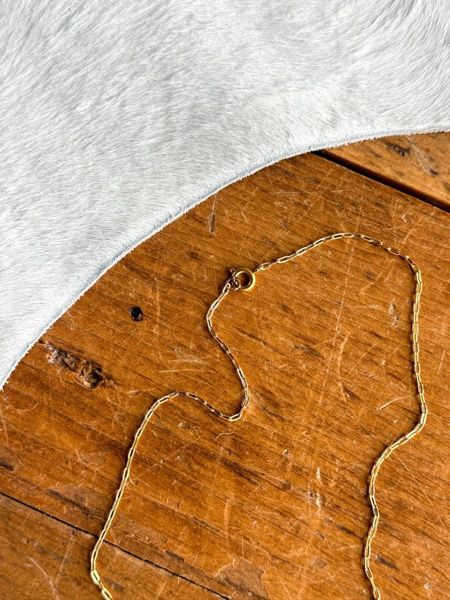 The Niota Necklace by Savannah Sevens western life{&}style features a delicate, tarnish-resistant 14k gold filled oval link chain with clasp, displayed on rustic wood beside soft gray cowhide—adding elegance to any style.