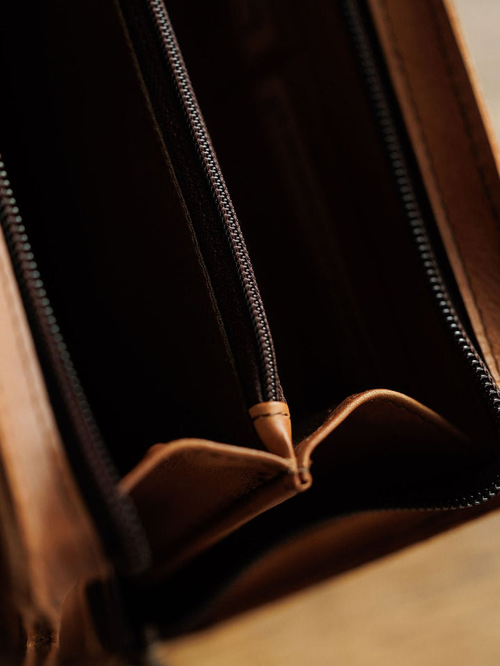 Close-up of an empty Nocona Leather Crossbody Wallet by Savannah Sevens western life{&}style, made from brown full grain leather with open compartments and a visible zipper; no cash or cards inside.