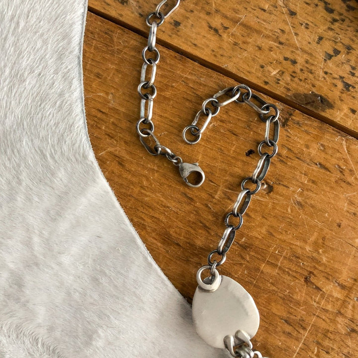 A close-up of the Nogales Necklace by Savannah Sevens western life{&}style, featuring sterling silver and a lobster clasp, displayed on wood beside white cowhide.