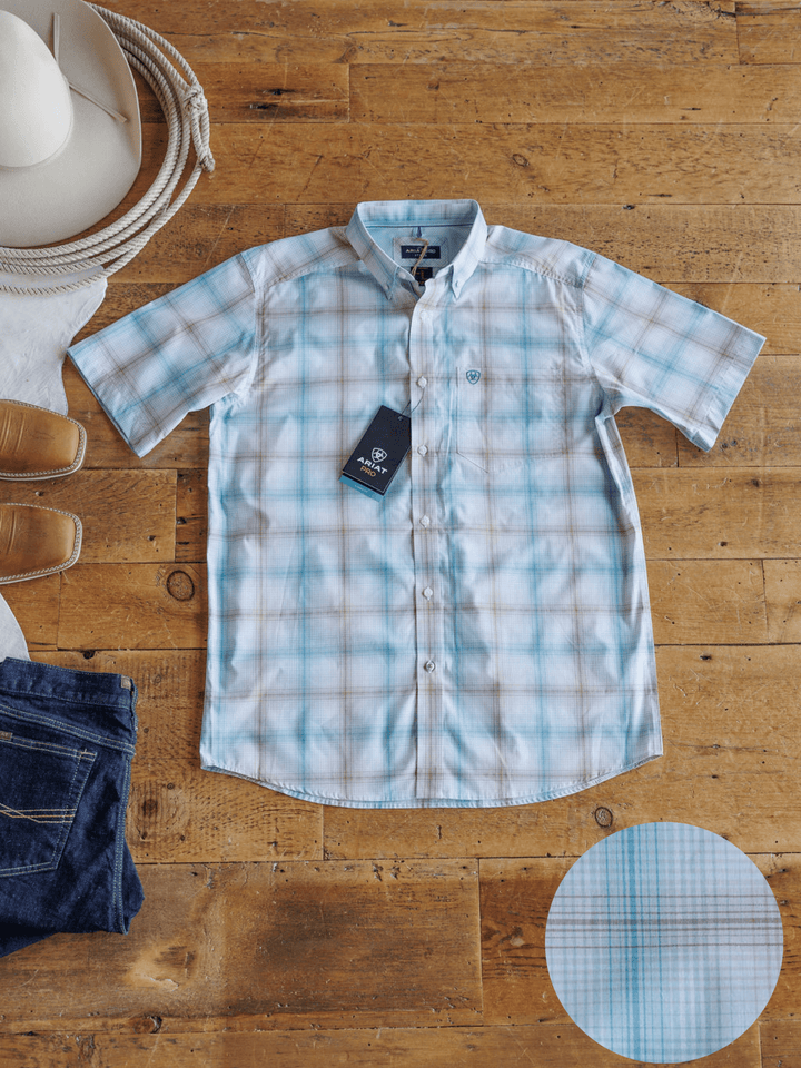 The Nolanville Ariat Men's Plaid Button Up by Savannah Sevens western life{&}style, in light blue and white, is laid flat with a white cowboy hat, tan shoes, blue jeans, and a close-up of the shirt’s fabric pattern.
