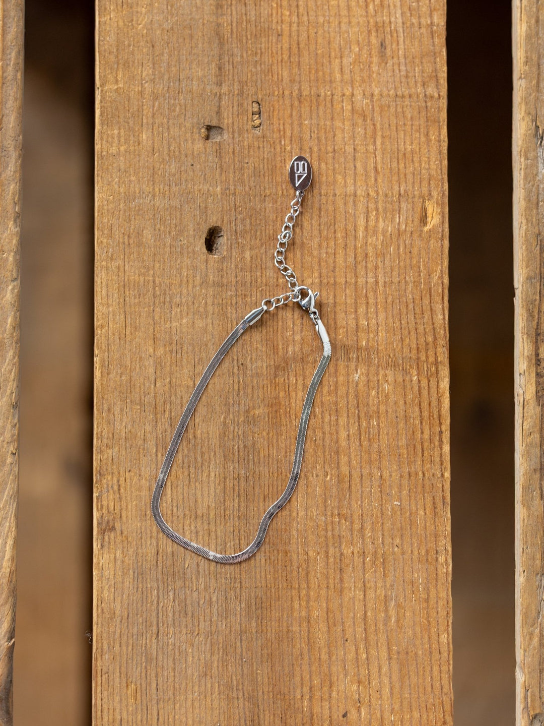 The Norvell Silver Herringbone Bracelet by Savannah Sevens western life{&}style rests on a wooden surface with visible grain and two holes.