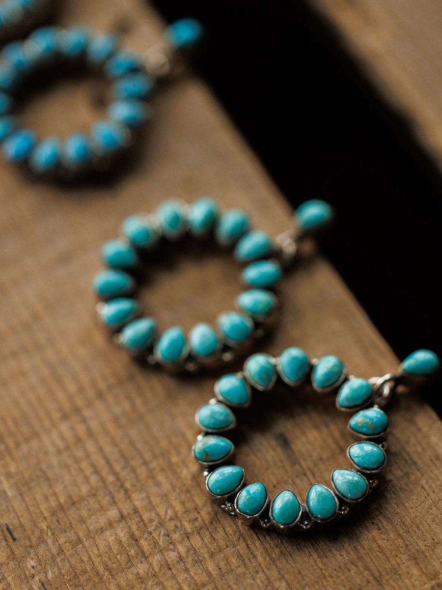 Close-up of three Ocala Earrings by Savannah Sevens western life{&}style—circular sterling silver pieces with Kingman turquoise stones, arranged diagonally on rustic wood. The centered earring is in sharp focus, while the others are gently blurred.