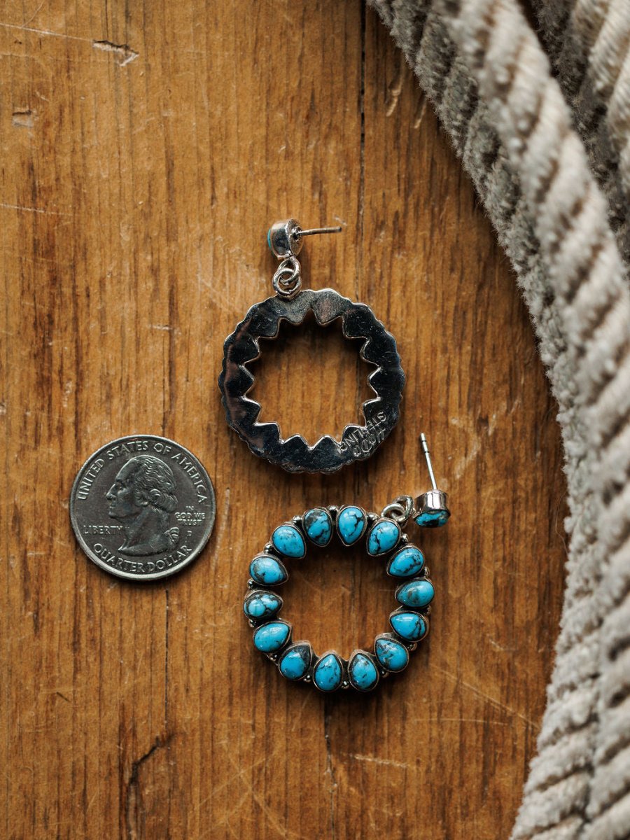 A U.S. quarter is next to Savannah Sevens western life{&}style Ocala Earrings—one shows the jagged sterling silver back, the other displays Kingman turquoise—set on wood near textured beige fabric.