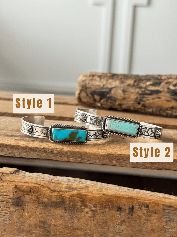 Two Ocala Turquoise Cuffs by Savannah Sevens western life{&}style are displayed on rustic wooden surfaces. One features a wide silver band with engraved patterns, while the other has a slightly thinner band with engraved designs and a rectangular Kingman turquoise stone.