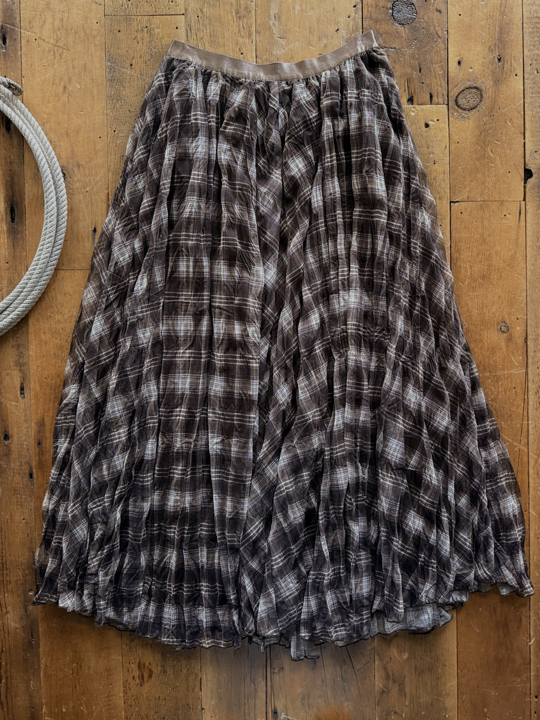 The Okeene Espresso Plaid Skirt is a high-waisted, espresso plaid midi skirt with a long, pleated design.