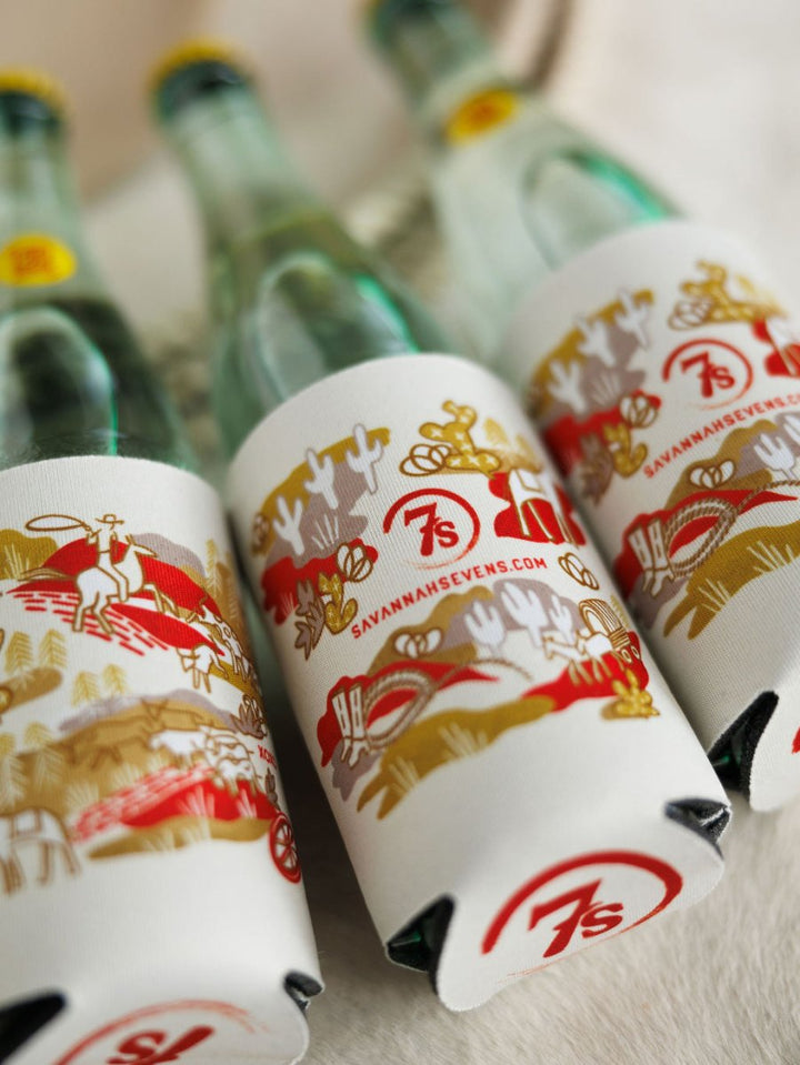 The Out West Koozie by Savannah Sevens western life{&}style features three glass bottles in colorful holders with hand-drawn cacti, horses, SAVANNAHSEVENS.COM text, and a red "7s" logo—adding Western flair to your drinkware.