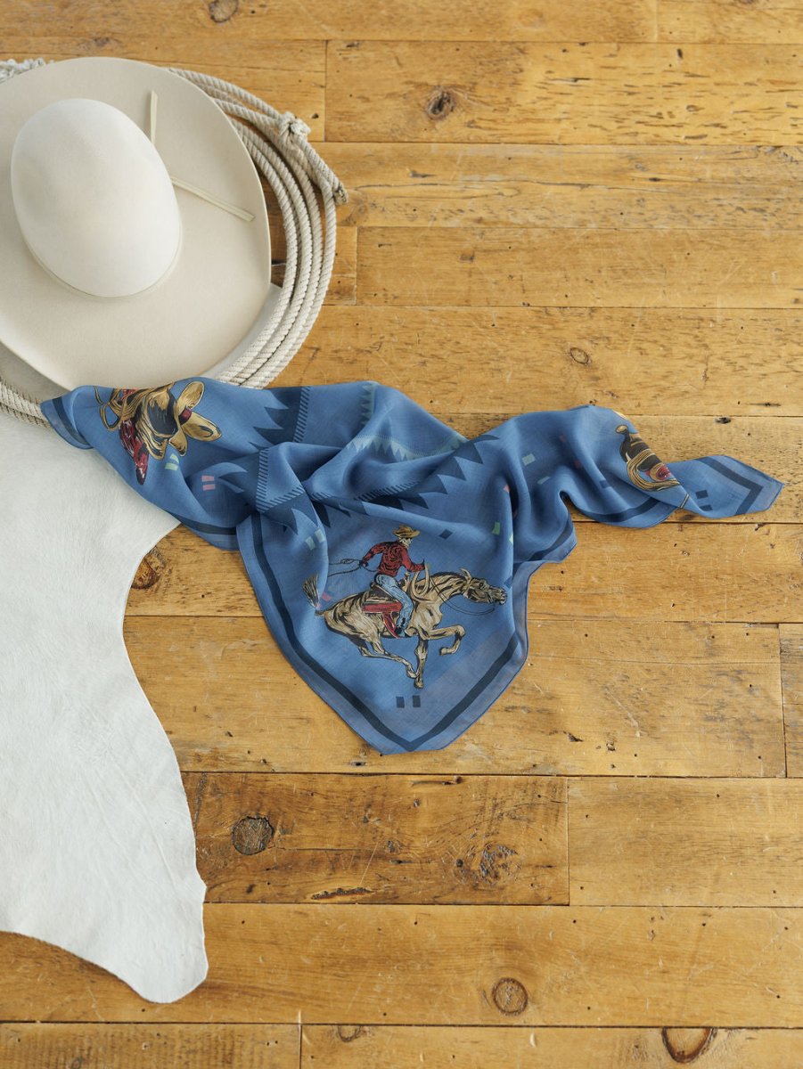 The Paducah Neck Scarf by Savannah Sevens western life{&}style, featuring cowboy and horse prints, rests on a wooden surface beside a white cowboy hat, coiled rope, and white leather.