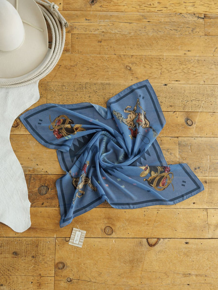 The Paducah Neck Scarf by Savannah Sevens western life{&}style, featuring blue chiffon and Western-themed graphics, is displayed on wood with a white cowboy hat, coiled rope, white cloth, and a small tag beside the neck scarf.