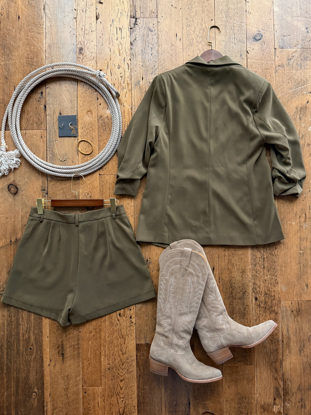 The Pagosa Olive Blazer Set, featuring an olive green blazer and matching relaxed-fit high-waisted shorts, styled with light tan western boots and jewelry on a wooden floor.