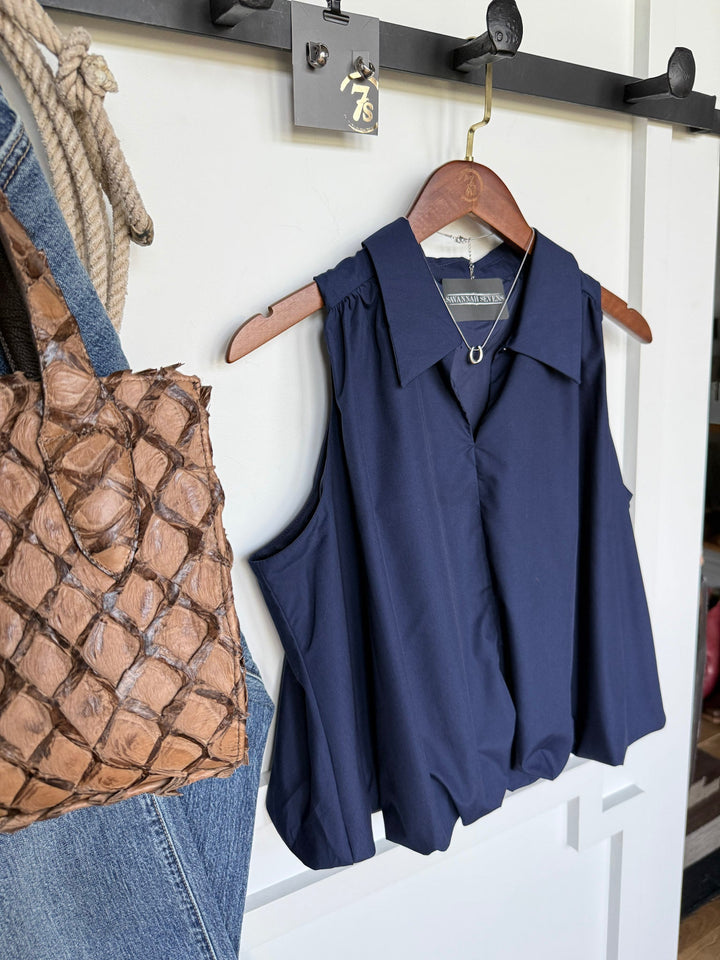 The Panora Navy Bubble Hem Top by Savannah Sevens western life{&}style hangs on a wooden hanger from a black wall rack. Beside it are a woven brown bag and a pair of blue jeans. A small tag with the number 75 hangs above the top, ideal for those looking for young contemporary sizing.