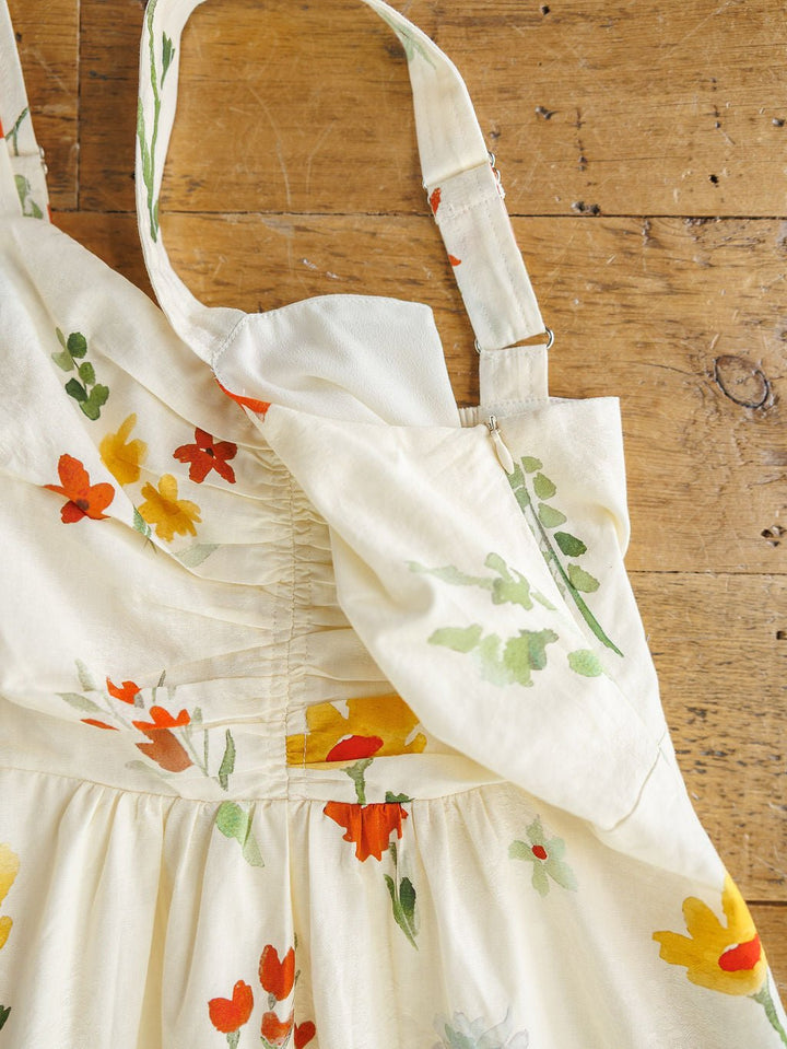 The Park Floral Dress by Savannah Sevens western life{&}style is a cotton sleeveless midi dress with adjustable straps, subtle pleats, a bow detail at the top, and a red, yellow, and green spring floral print.