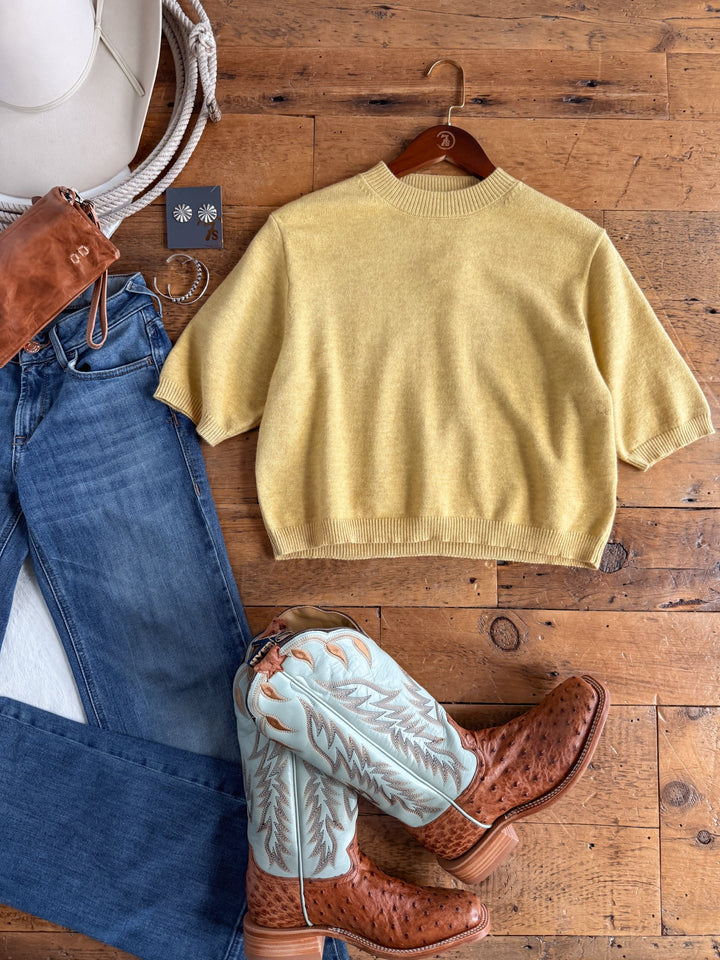 Flat lay of the Pasadena Yellow Chartreuse Knit Top by Savannah Sevens western life{&}style, paired with blue jeans, turquoise and brown cowboy boots, a brown purse, a white cowboy hat, coiled rope, and silver earrings displayed on a wooden floor.
