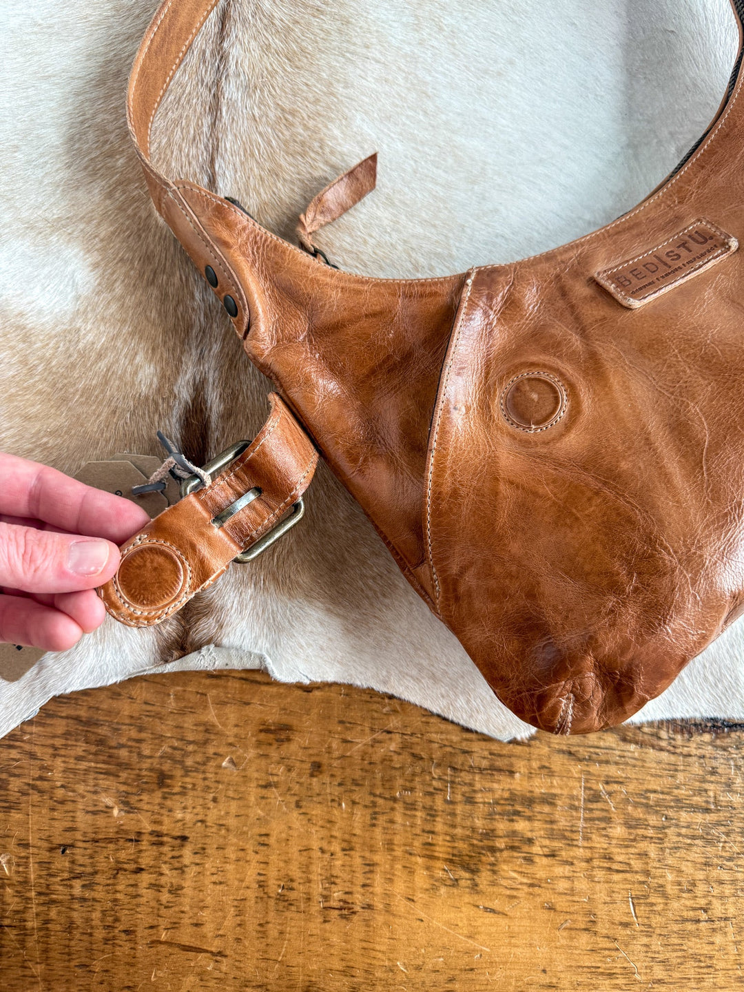 A hand fastens the buckle on a Savannah Sevens western life{&}style Pasco Leather Handbag resting on a tan cowhide and wooden surface.